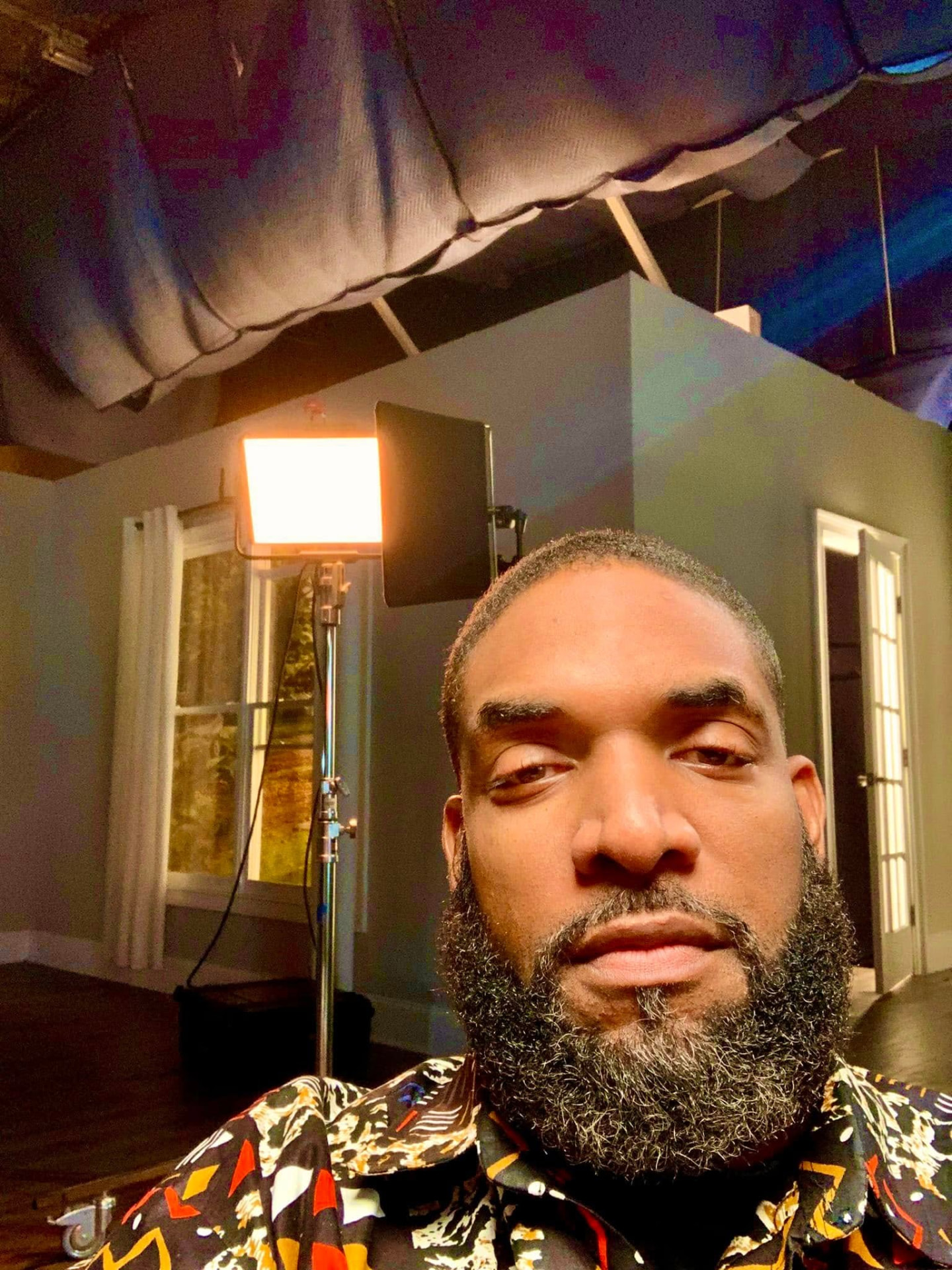 Jay Cameron on a lit set with a studio light and a built room behind him