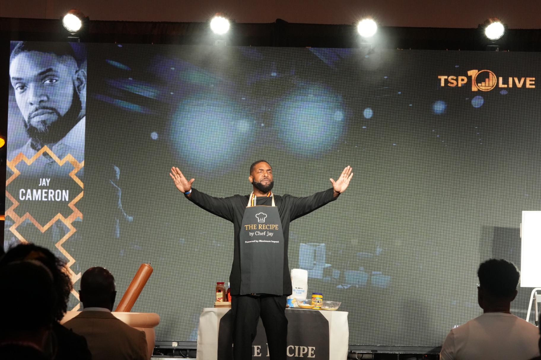 Jay Cameron on stage with arms open in front of a large screen