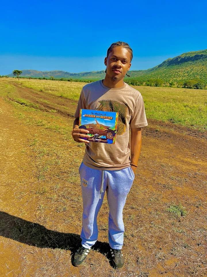 A young man holding the Darren and Destiny book on a dirt road across open grassland
