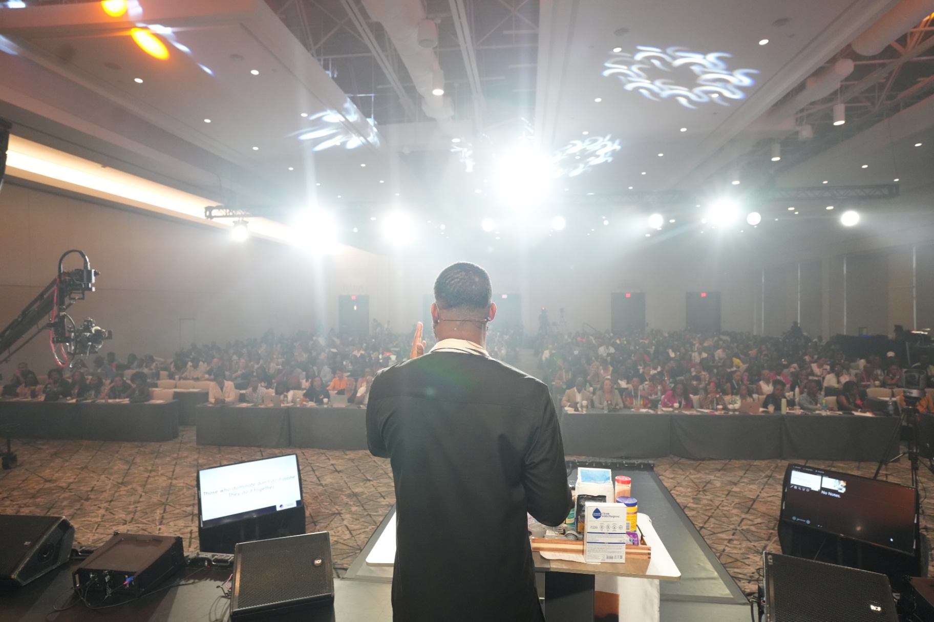 Jay Cameron on a main stage under the lights, addressing a packed ballroom