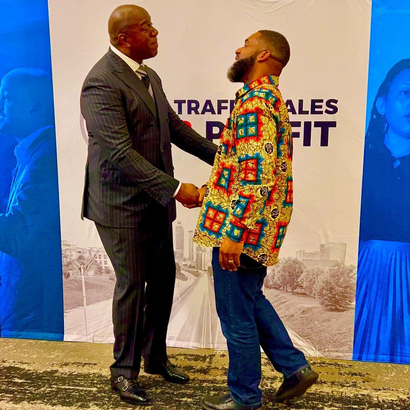 Jay Cameron shaking hands with a guest in front of a business conference backdrop