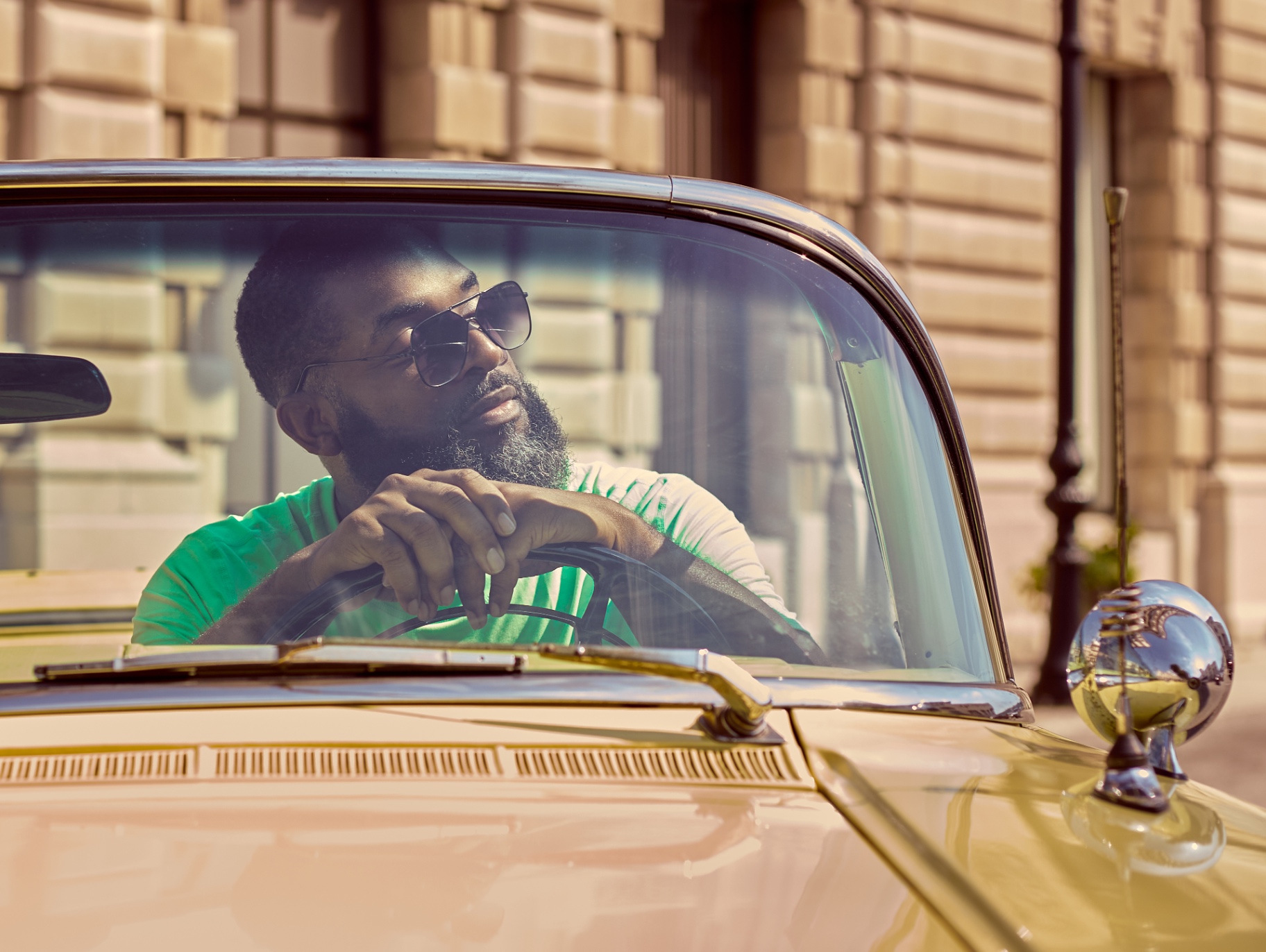 Jay Cameron behind the wheel of a classic convertible on a sunlit street