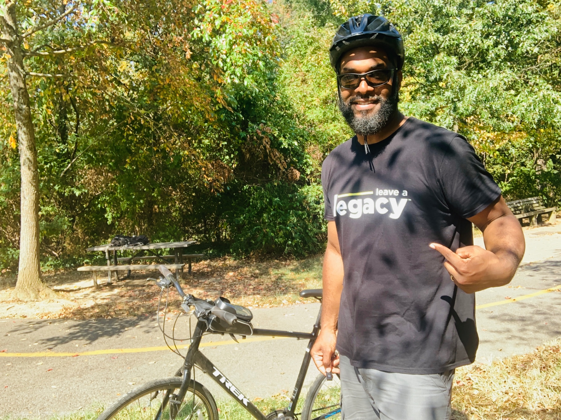 Jay Cameron on a wooded trail with his bike, wearing a Leave a Legacy shirt